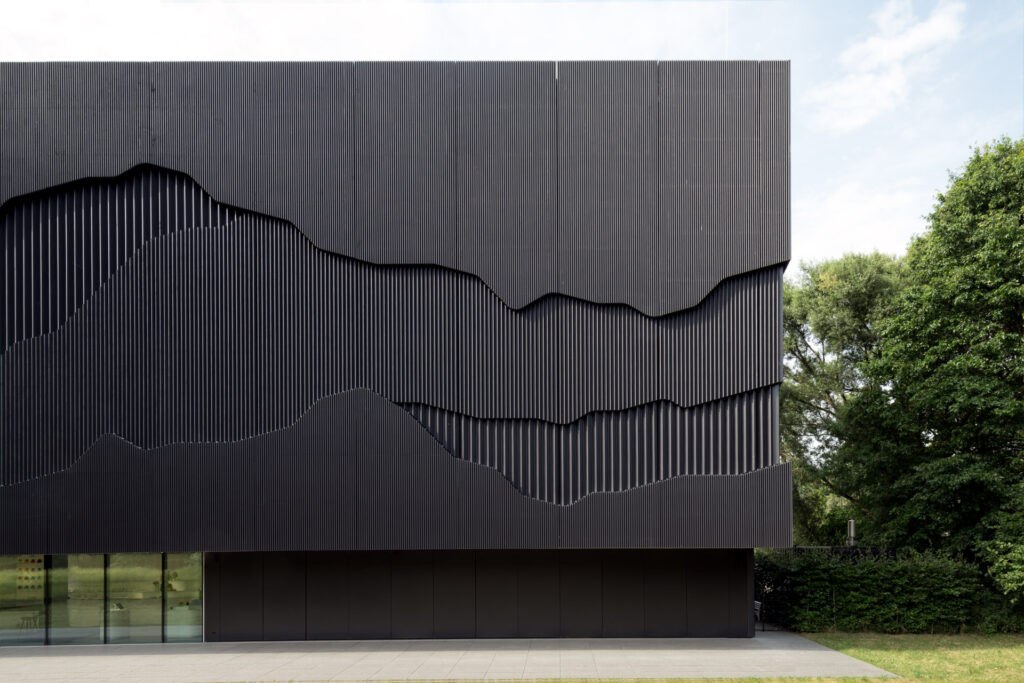 Fine art architectural detail of a dark corrugated metal building facade with organic wave-cut relief shapes