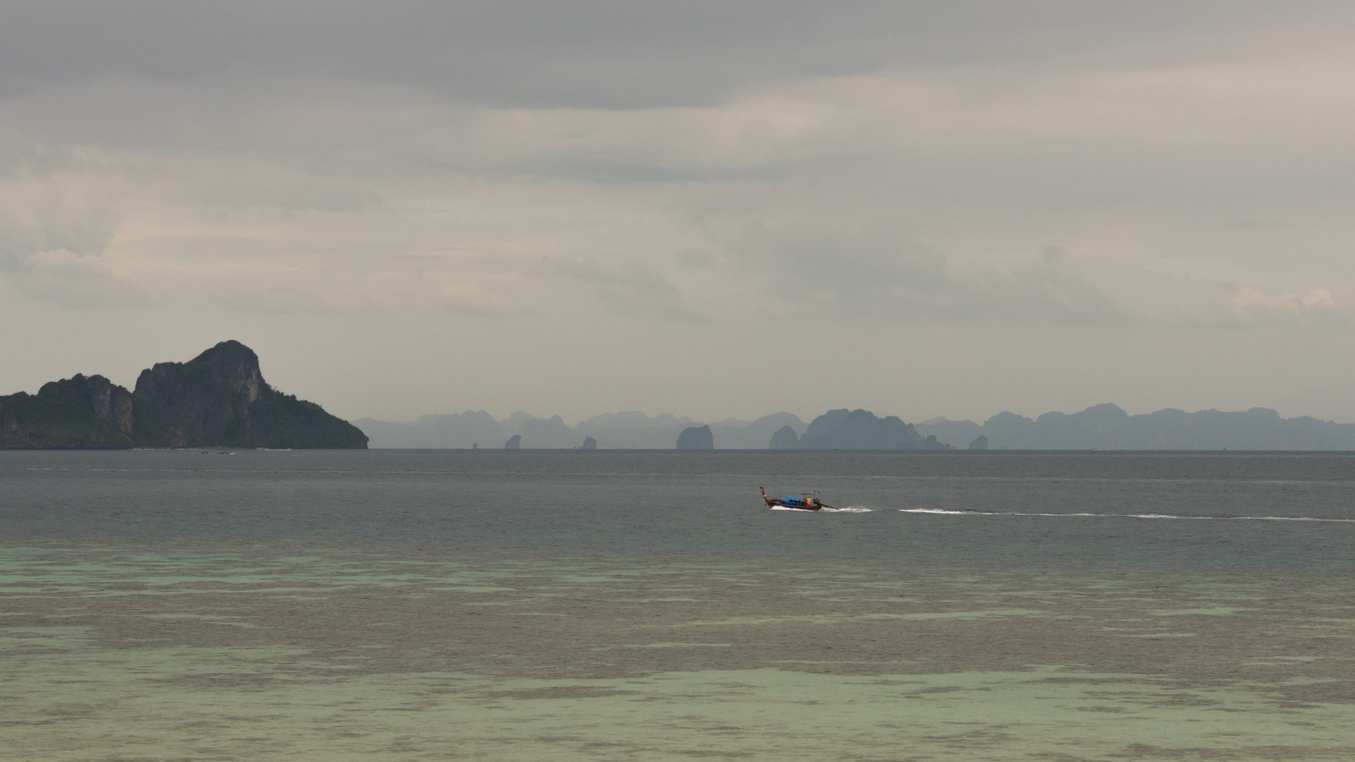 A longtail boat at Phi Phi Island, surrounded by cloudy skies, reflecting the serene atmosphere of the coastal landscape.
