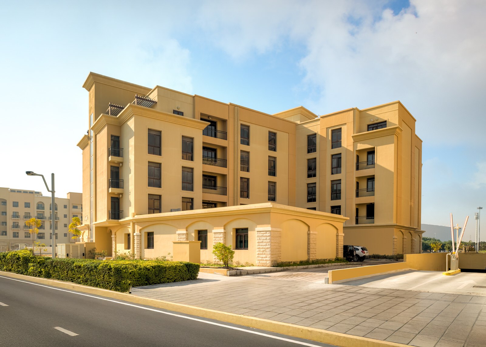 Modern multi-story apartment building in warm beige tones with balconies and landscaped surroundings under a sunny sky