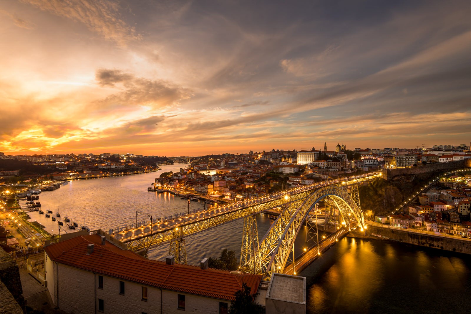 A stunning sunset over Porto, showcasing the illuminated Dom Luís I Bridge and the Douro River lined with colorful buildings.