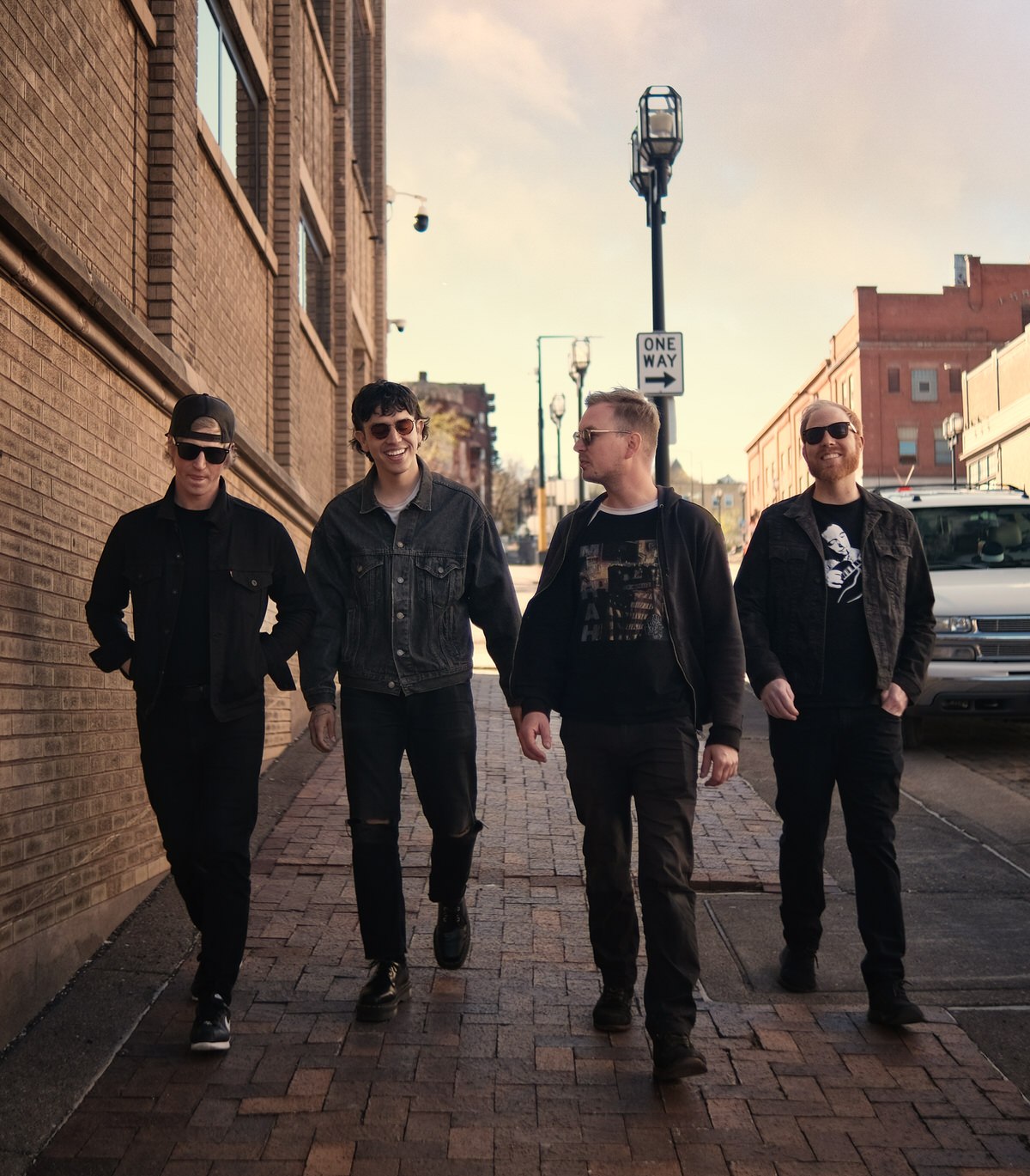 four bandmembers walking down a street during sunset next to an old building
