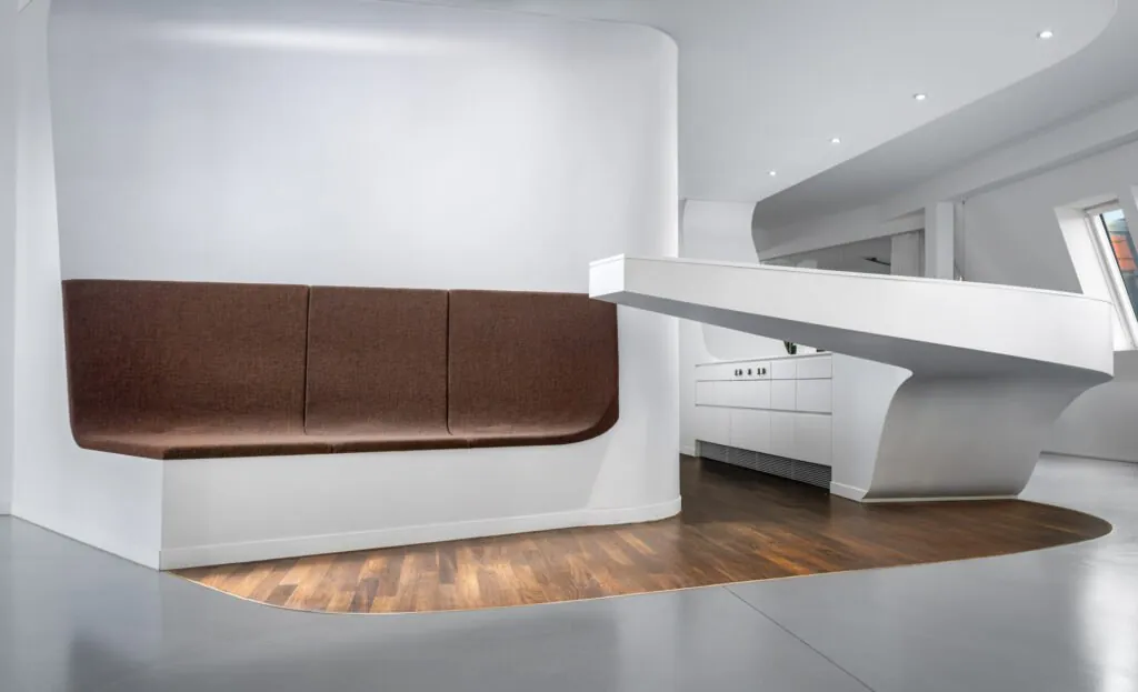 Architecturally designed white kitchen island with sweeping curved forms, warm wood flooring, and a large skylight
