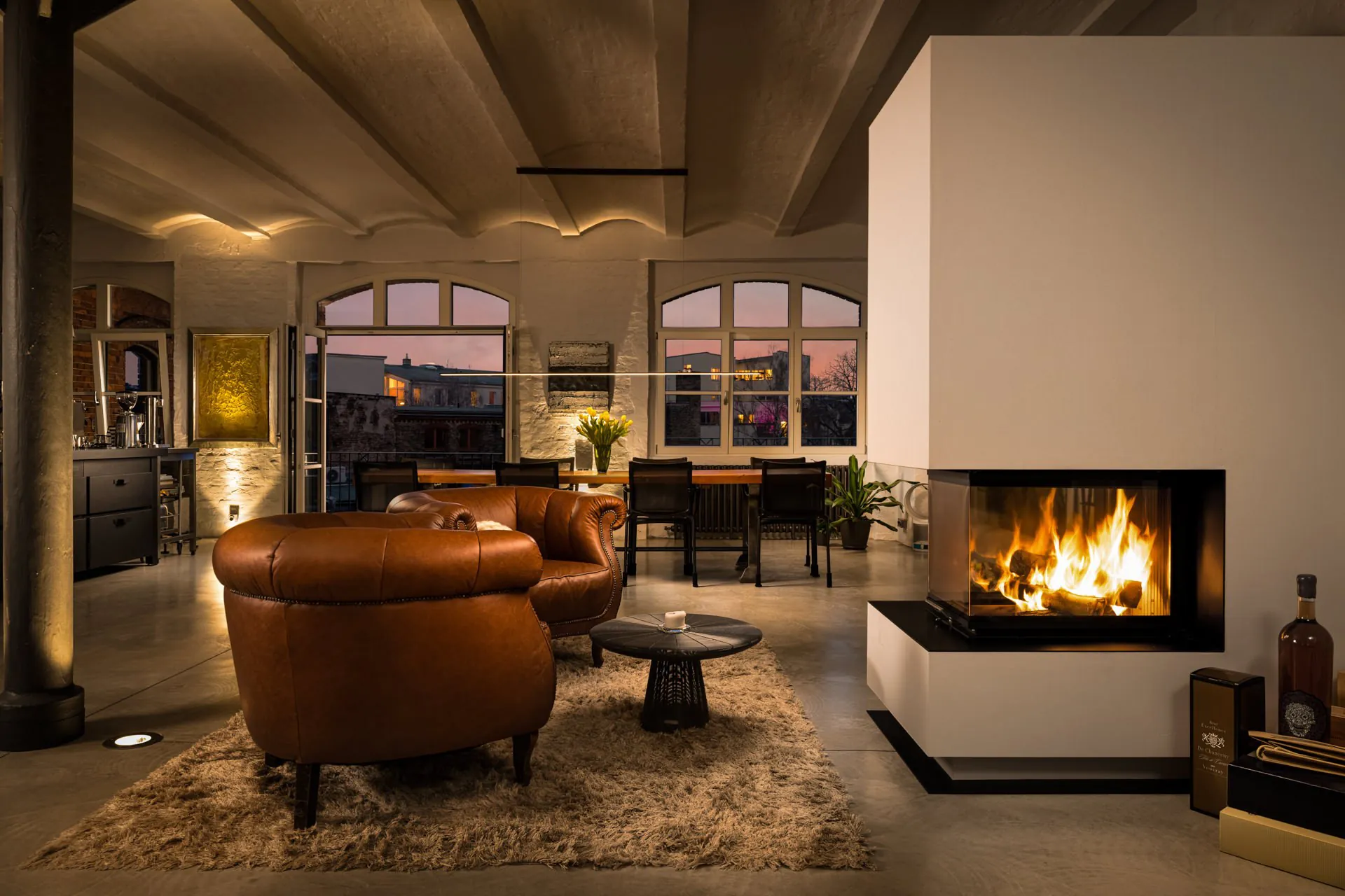 Warm living room with an open fireplace, leather club chairs, and soft evening ambient lighting