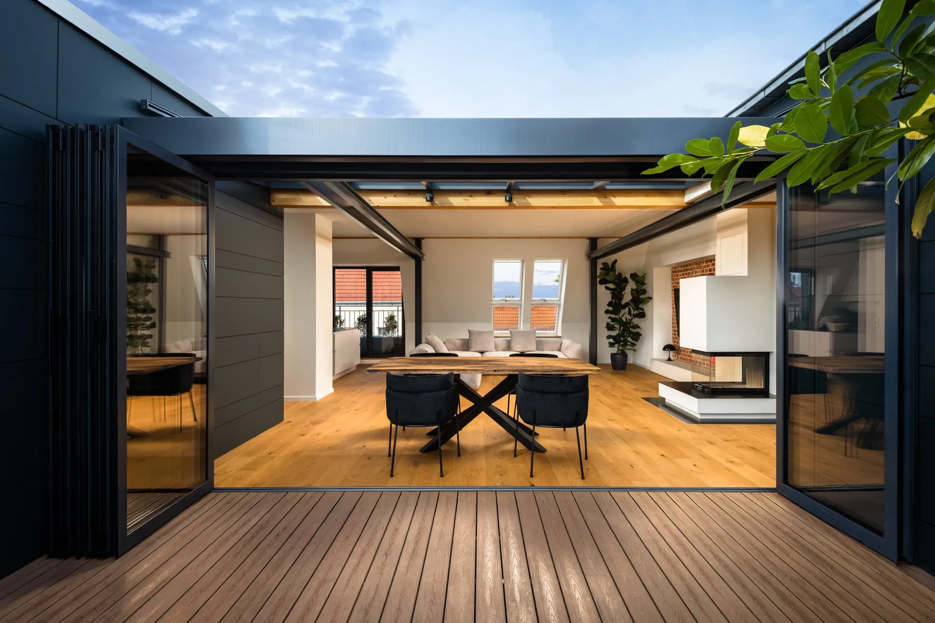 View from a rooftop terrace into a loft living room through large glass sliding doors with dark steel framing